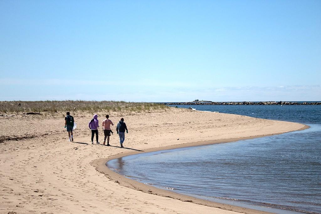 Four U N E students walking down the beach next to the ocean