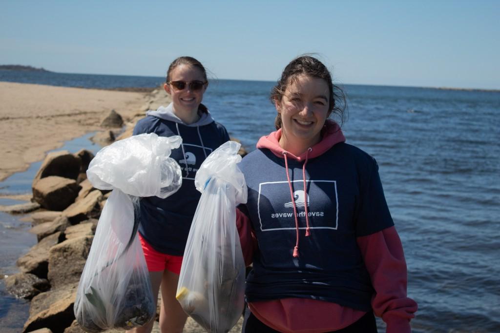 两个学生在清理海滩时举着垃圾袋