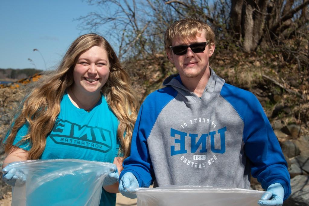 两名学生微笑着举着垃圾袋参加“拯救海浪”清理活动