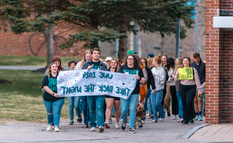 一群学生在校园里游行，举着一个标语，上面写着“正规澳门赌场网络2024年夺回夜晚”。